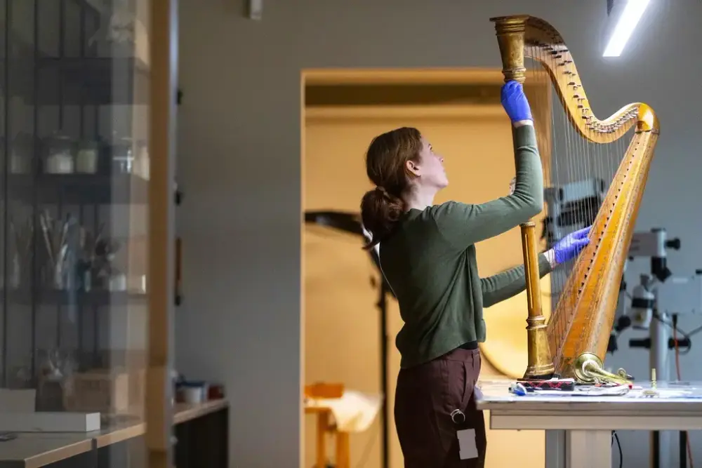 Person med hansker holder forsiktig i en harpe på et laboratorium. Foto. 