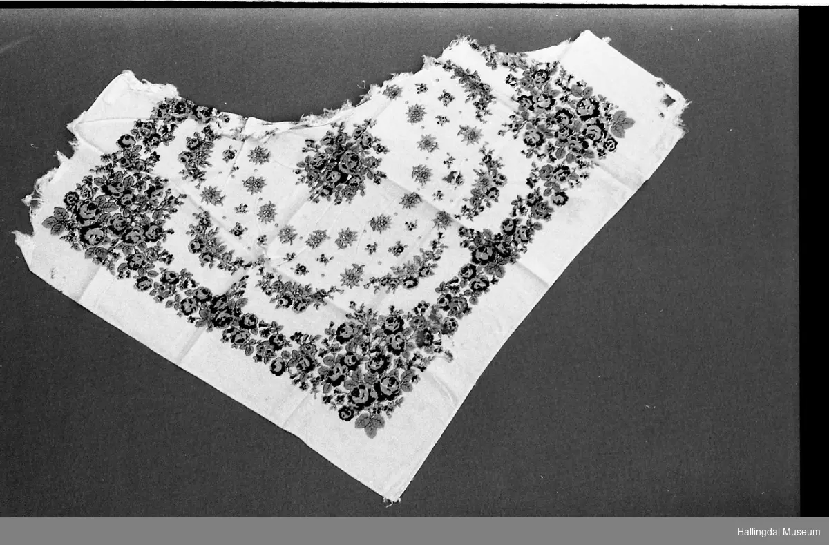 Tørkle. Hvit bunn med trykt rosemønster i blått, grønt, rødt  og gult. Svært slitt og fillete. 1/3 borte.