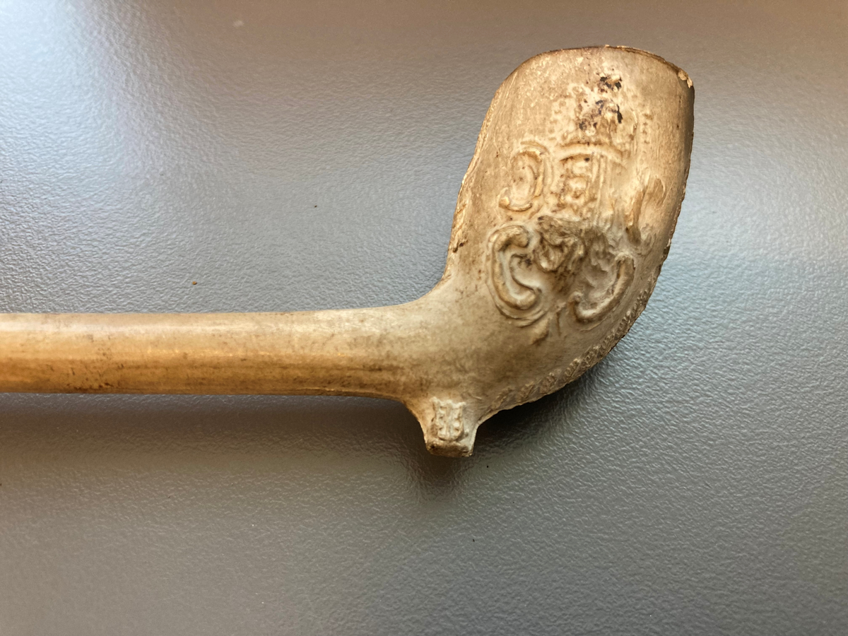 Krittpipe, dekor på pipehode (våpenskjold og et hode) 1700-talls. Hvit med rødt munnparti.