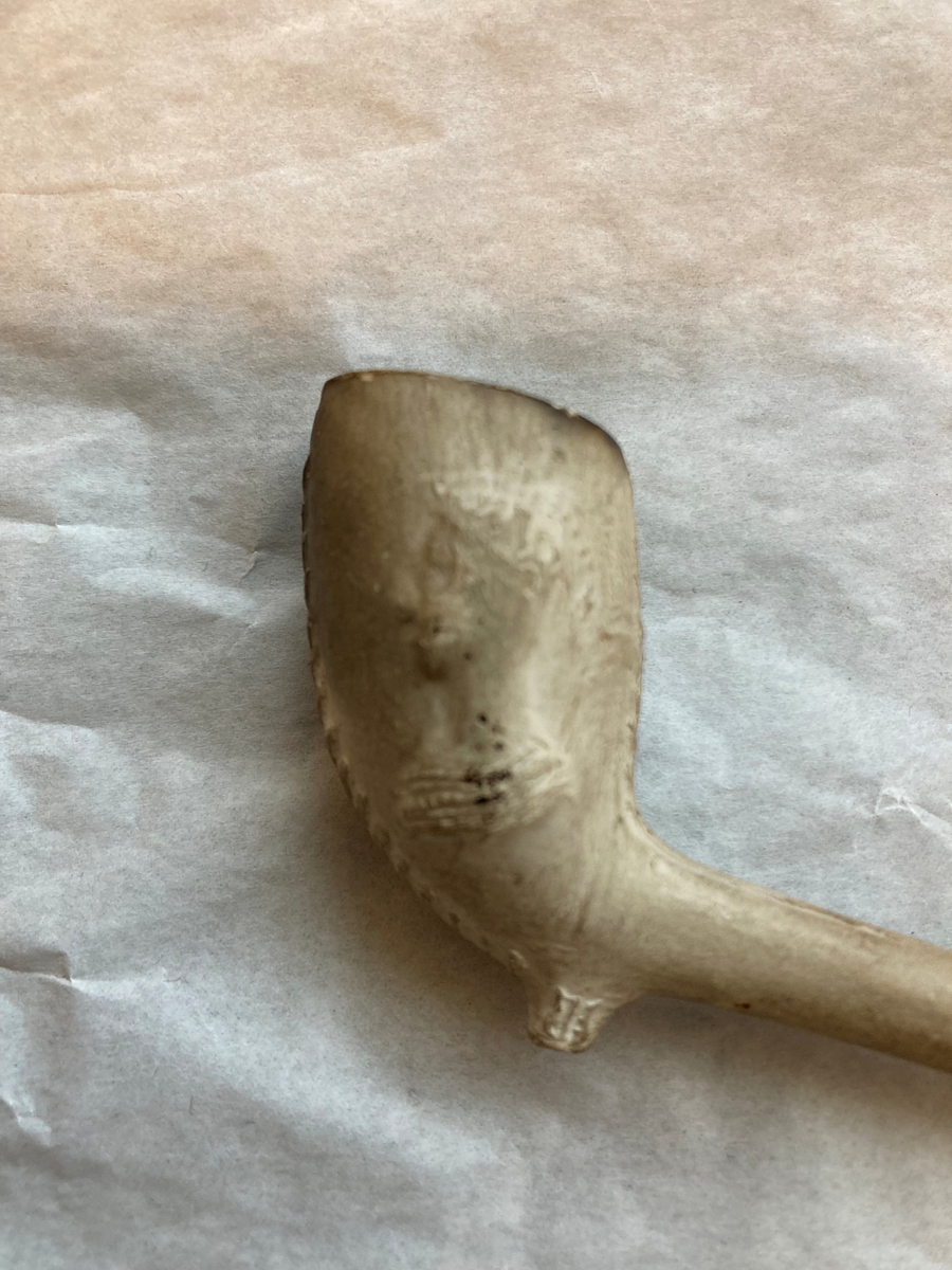 Krittpipe, dekor på pipehode (våpenskjold og et hode) 1700-talls. Hvit med rødt munnparti.