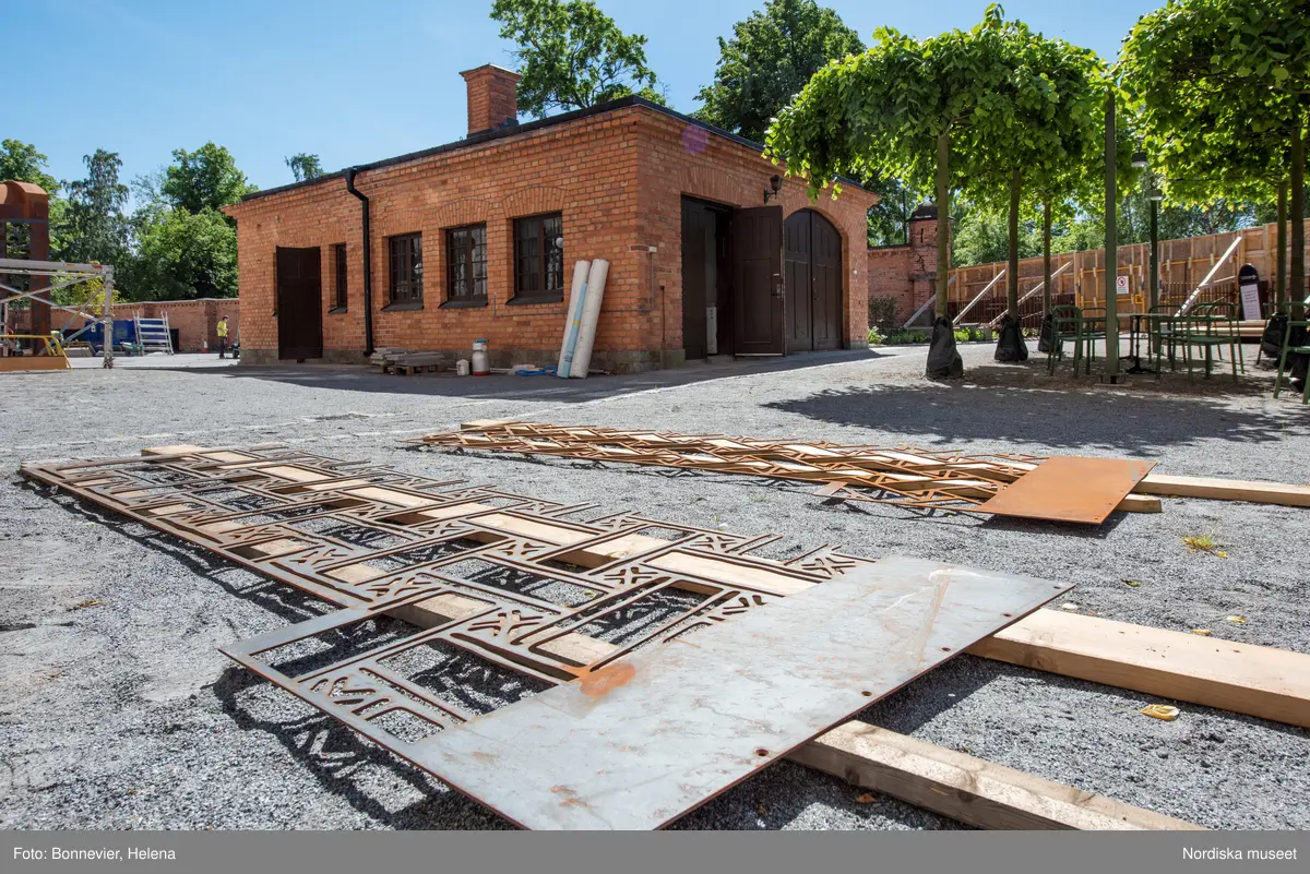 Exteriörer från Nordiska museets västra sida, bakgården, under arbetet med den nya entrén och byggnaden Lusknäppen. Entrén är ritad av Lone-Pia Bach. Konstnären Outi Pieski står för den konstnärliga gestaltningen med konstverket Two Directions, inspirerat av föremål ur museets samiska samlingar. På marken ligger rostiga delar till utbyggnaden, tulpanerna blommar.