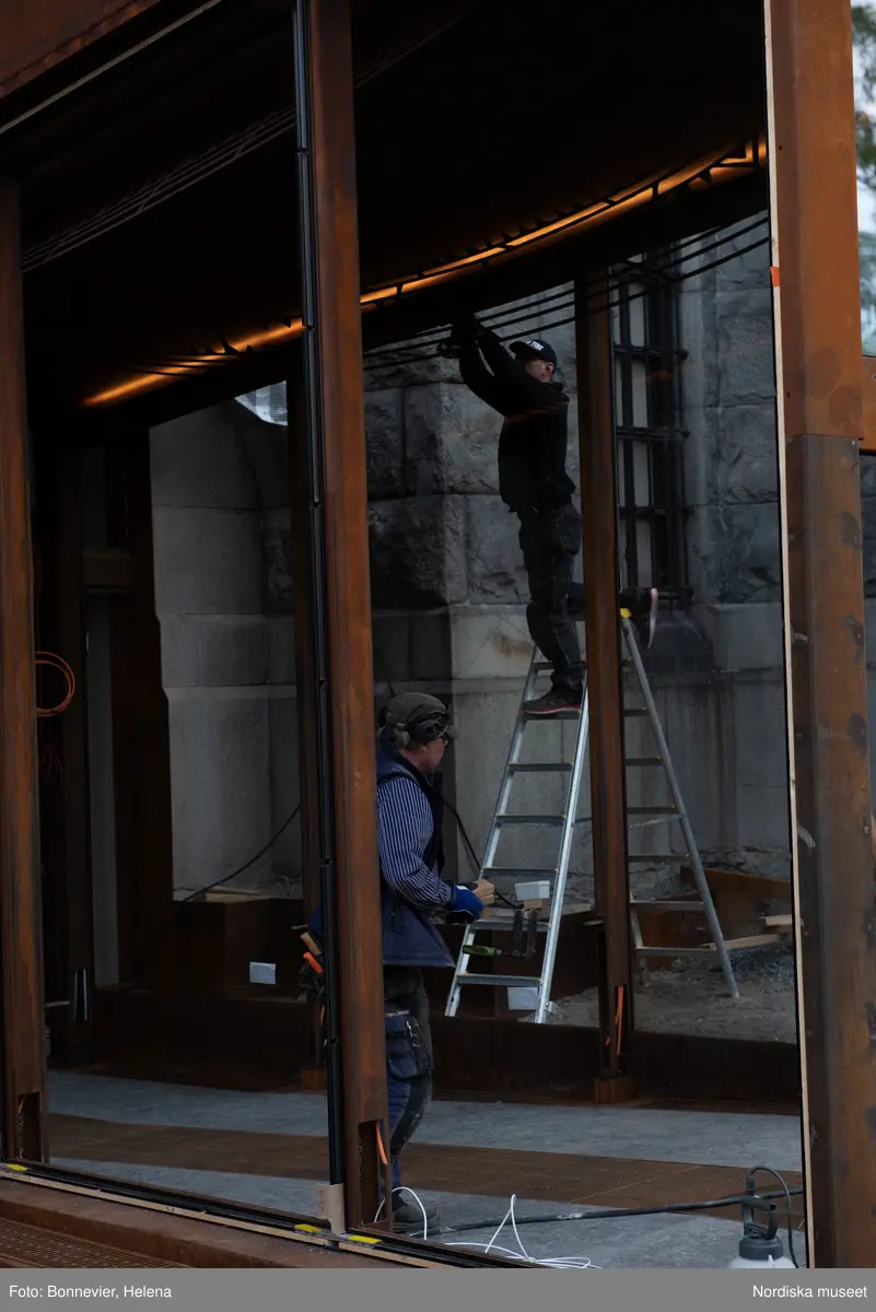 Exteriörer från Nordiska museets västra sida, bakgården, under arbetet med den nya entrén och byggnaden Lusknäppen. Entrén är ritad av Lone-Pia Bach. Konstnären Outi Pieski står för den konstnärliga gestaltningen med konstverket Two Directions, inspirerat av föremål ur museets samiska samlingar. Montering av glaset i utbyggnaden.