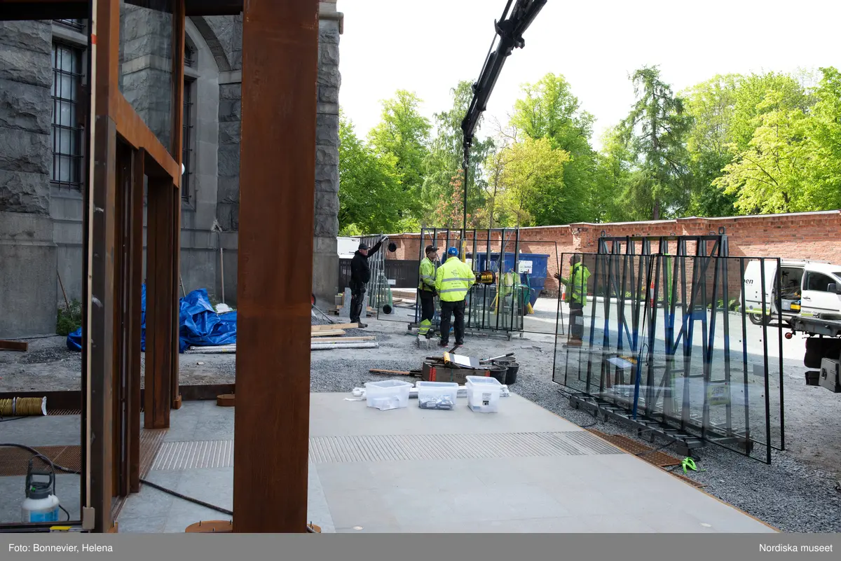 Exteriörer från Nordiska museets västra sida, bakgården, under arbetet med den nya entrén och byggnaden Lusknäppen. Entrén är ritad av Lone-Pia Bach. Konstnären Outi Pieski står för den konstnärliga gestaltningen med konstverket Two Directions, inspirerat av föremål ur museets samiska samlingar. Montering av glaset i utbyggnaden.