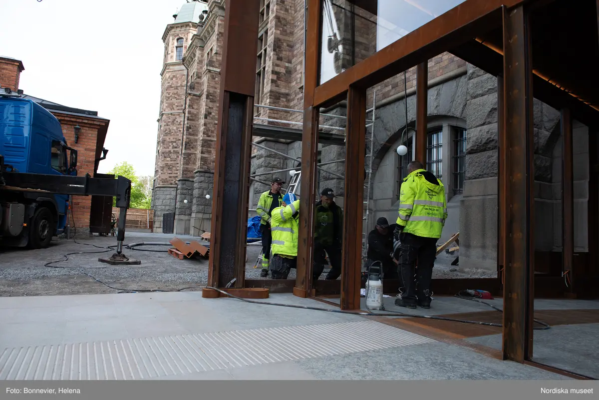 Exteriörer från Nordiska museets västra sida, bakgården, under arbetet med den nya entrén och byggnaden Lusknäppen. Entrén är ritad av Lone-Pia Bach. Konstnären Outi Pieski står för den konstnärliga gestaltningen med konstverket Two Directions, inspirerat av föremål ur museets samiska samlingar. Montering av glaset i utbyggnaden.