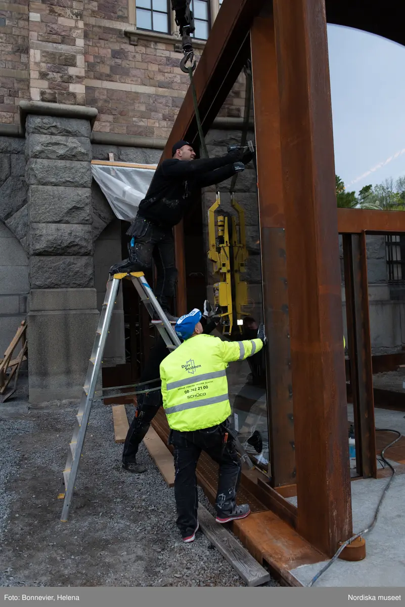 Exteriörer från Nordiska museets västra sida, bakgården, under arbetet med den nya entrén och byggnaden Lusknäppen. Entrén är ritad av Lone-Pia Bach. Konstnären Outi Pieski står för den konstnärliga gestaltningen med konstverket Two Directions, inspirerat av föremål ur museets samiska samlingar. Montering av glaset i utbyggnaden.