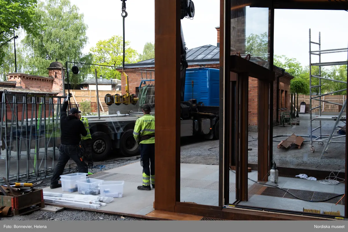 Exteriörer från Nordiska museets västra sida, bakgården, under arbetet med den nya entrén och byggnaden Lusknäppen. Entrén är ritad av Lone-Pia Bach. Konstnären Outi Pieski står för den konstnärliga gestaltningen med konstverket Two Directions, inspirerat av föremål ur museets samiska samlingar. Montering av glaset i utbyggnaden.