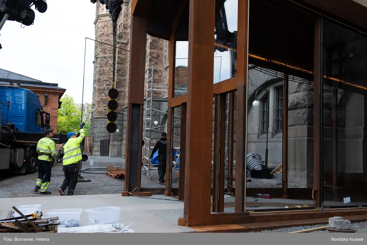 Exteriörer från Nordiska museets västra sida, bakgården, under arbetet med den nya entrén och byggnaden Lusknäppen. Entrén är ritad av Lone-Pia Bach. Konstnären Outi Pieski står för den konstnärliga gestaltningen med konstverket Two Directions, inspirerat av föremål ur museets samiska samlingar. Montering av glaset i utbyggnaden.