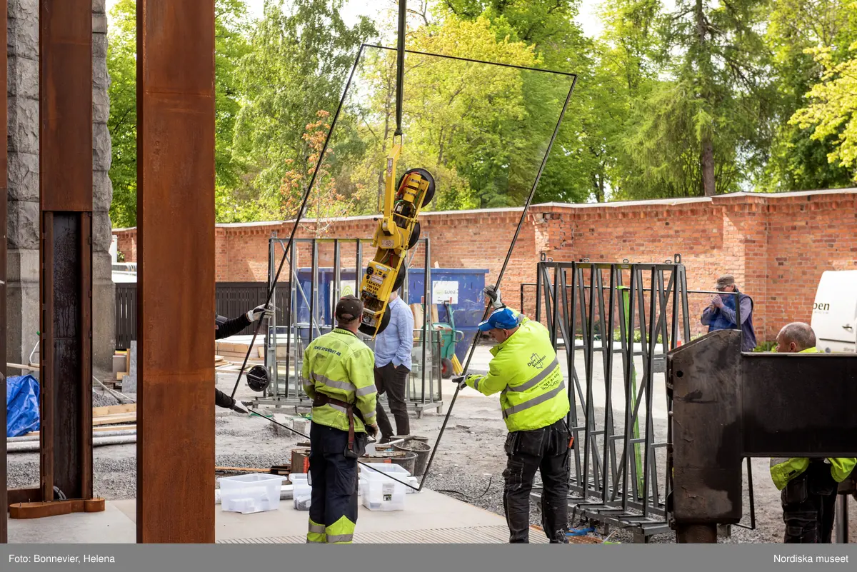 Exteriörer från Nordiska museets västra sida, bakgården, under arbetet med den nya entrén och byggnaden Lusknäppen. Entrén är ritad av Lone-Pia Bach. Konstnären Outi Pieski står för den konstnärliga gestaltningen med konstverket Two Directions, inspirerat av föremål ur museets samiska samlingar. Montering av glaset i utbyggnaden.