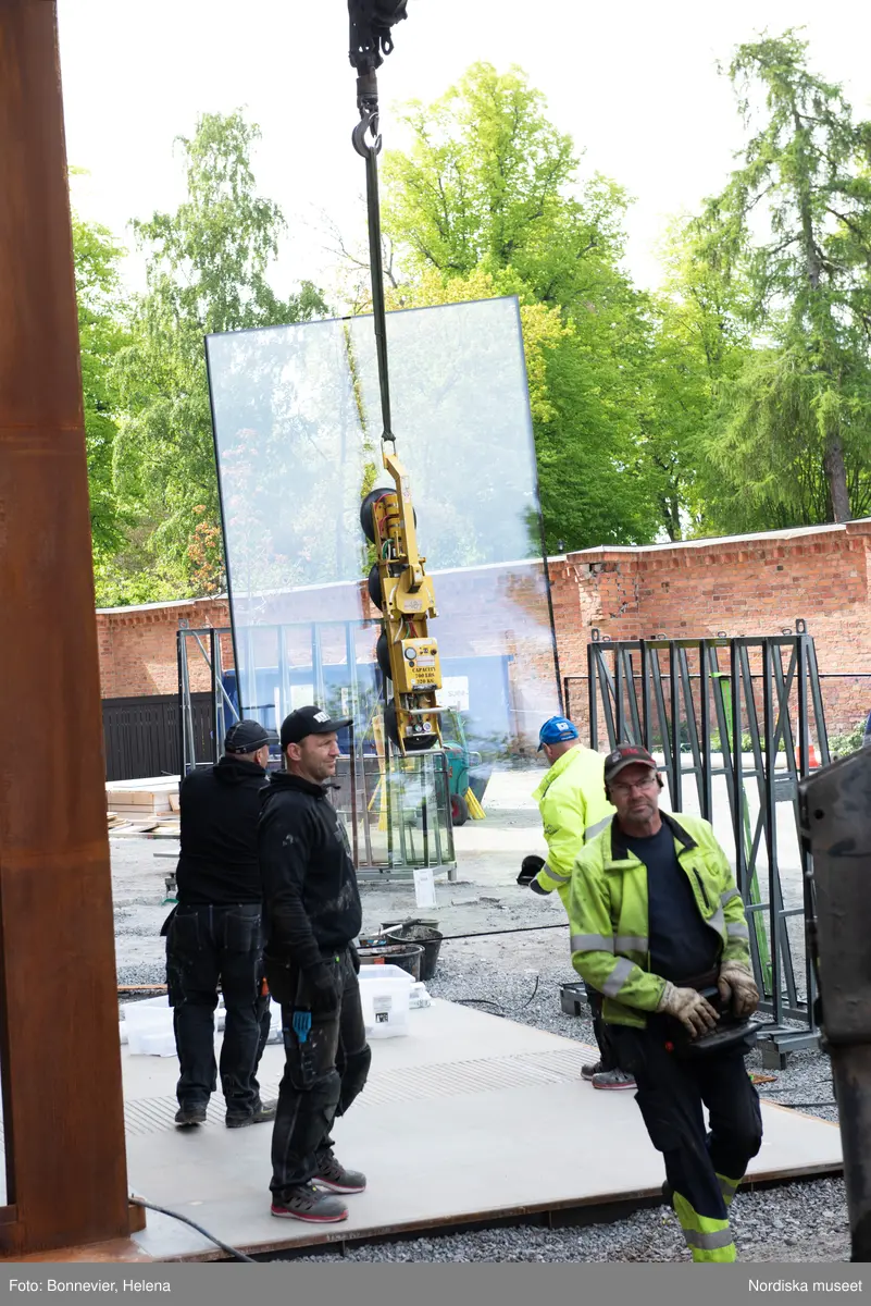 Exteriörer från Nordiska museets västra sida, bakgården, under arbetet med den nya entrén och byggnaden Lusknäppen. Entrén är ritad av Lone-Pia Bach. Konstnären Outi Pieski står för den konstnärliga gestaltningen med konstverket Two Directions, inspirerat av föremål ur museets samiska samlingar. Montering av glaset i utbyggnaden.