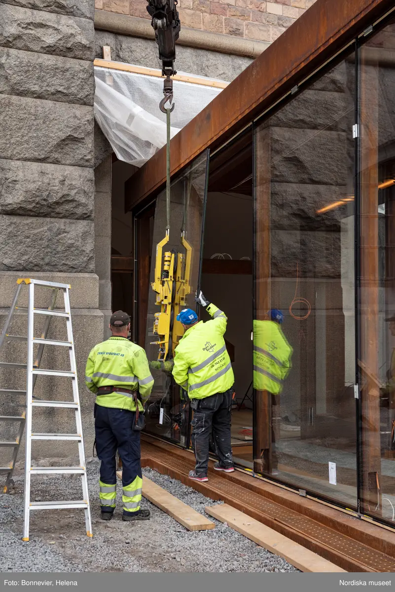 Exteriörer från Nordiska museets västra sida, bakgården, under arbetet med den nya entrén och byggnaden Lusknäppen. Entrén är ritad av Lone-Pia Bach. Konstnären Outi Pieski står för den konstnärliga gestaltningen med konstverket Two Directions, inspirerat av föremål ur museets samiska samlingar. Montering av glaset i utbyggnaden.