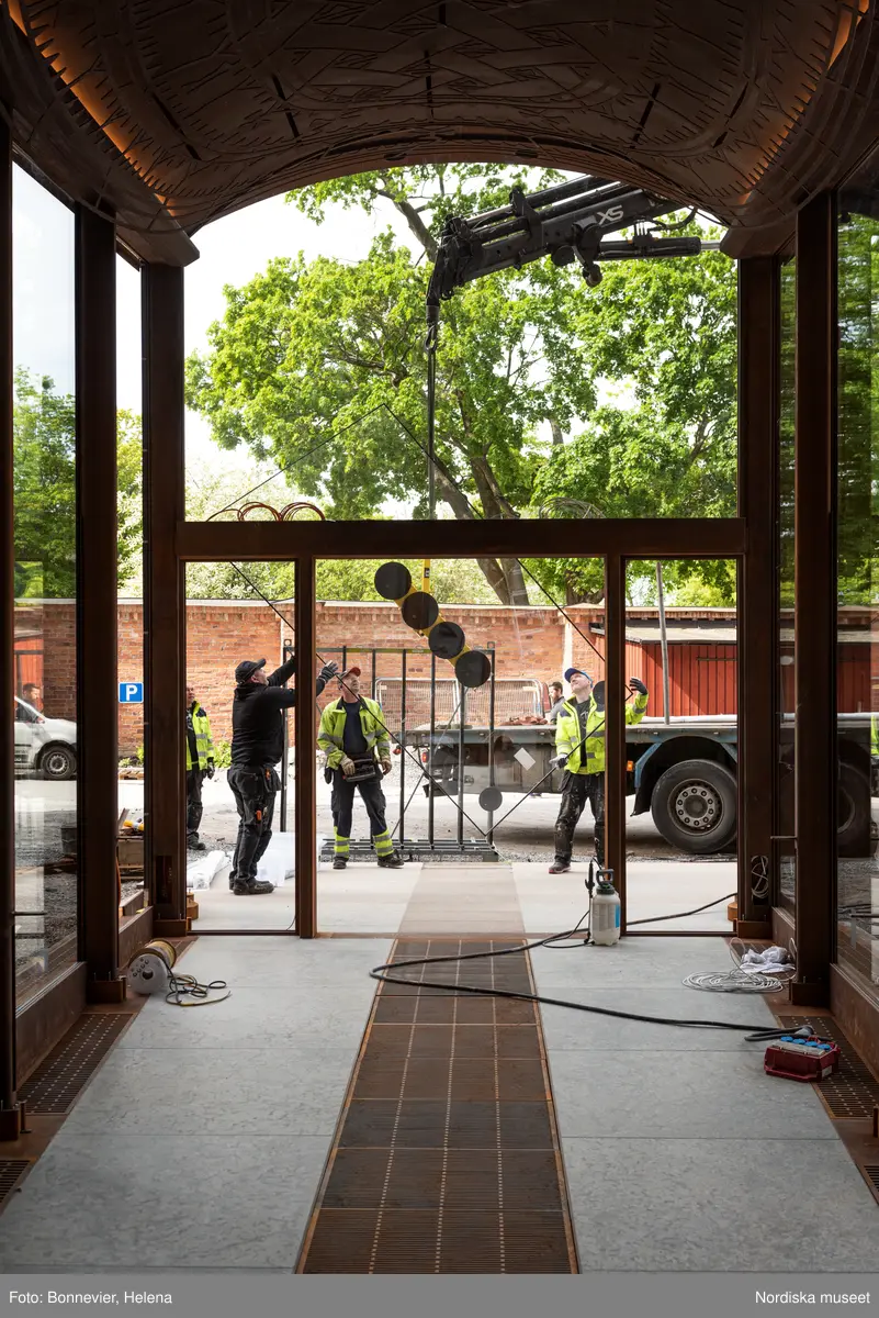 Exteriörer från Nordiska museets västra sida, bakgården, under arbetet med den nya entrén och byggnaden Lusknäppen. Entrén är ritad av Lone-Pia Bach. Konstnären Outi Pieski står för den konstnärliga gestaltningen med konstverket Two Directions, inspirerat av föremål ur museets samiska samlingar. Montering av glaset i utbyggnaden.