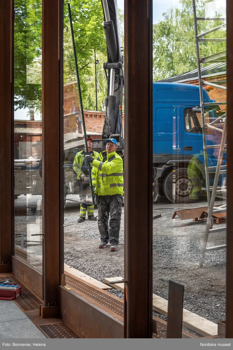 Exteriörer från Nordiska museets västra sida, bakgården, under arbetet med den nya entrén och byggnaden Lusknäppen. Entrén är ritad av Lone-Pia Bach. Konstnären Outi Pieski står för den konstnärliga gestaltningen med konstverket Two Directions, inspirerat av föremål ur museets samiska samlingar. Montering av glaset i utbyggnaden.