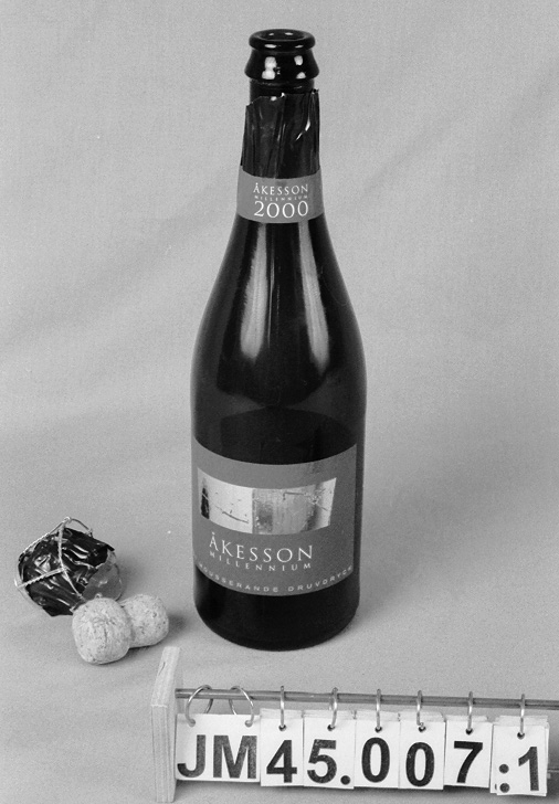Flaska av grönt glas för mousserande druvdryck, Blanc de Blancs, av färskpressade gröna druvor. Blå och guldfärgad etikett på framsidan med texten: "ÅKESSON MILLENNIUM SÖT MOUSSERANDE DRUVDRYCK". Etikett på baksidan med information om drycken samt på flaskhalsen med namnet på drycken. Flaska tom.