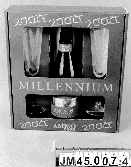 Flaska av grönt glas för mousserande druvdryck, Blanc de Blancs, av färskpressade gröna druvor. Blå och guldfärgad etikett på framsidan med texten: "ÅKESSON MILLENNIUM SÖT MOUSSERANDE DRUVDRYCK". Etikett på baksidan med information om drycken samt på flaskhalsen med namnet på drycken. Flaska tom.