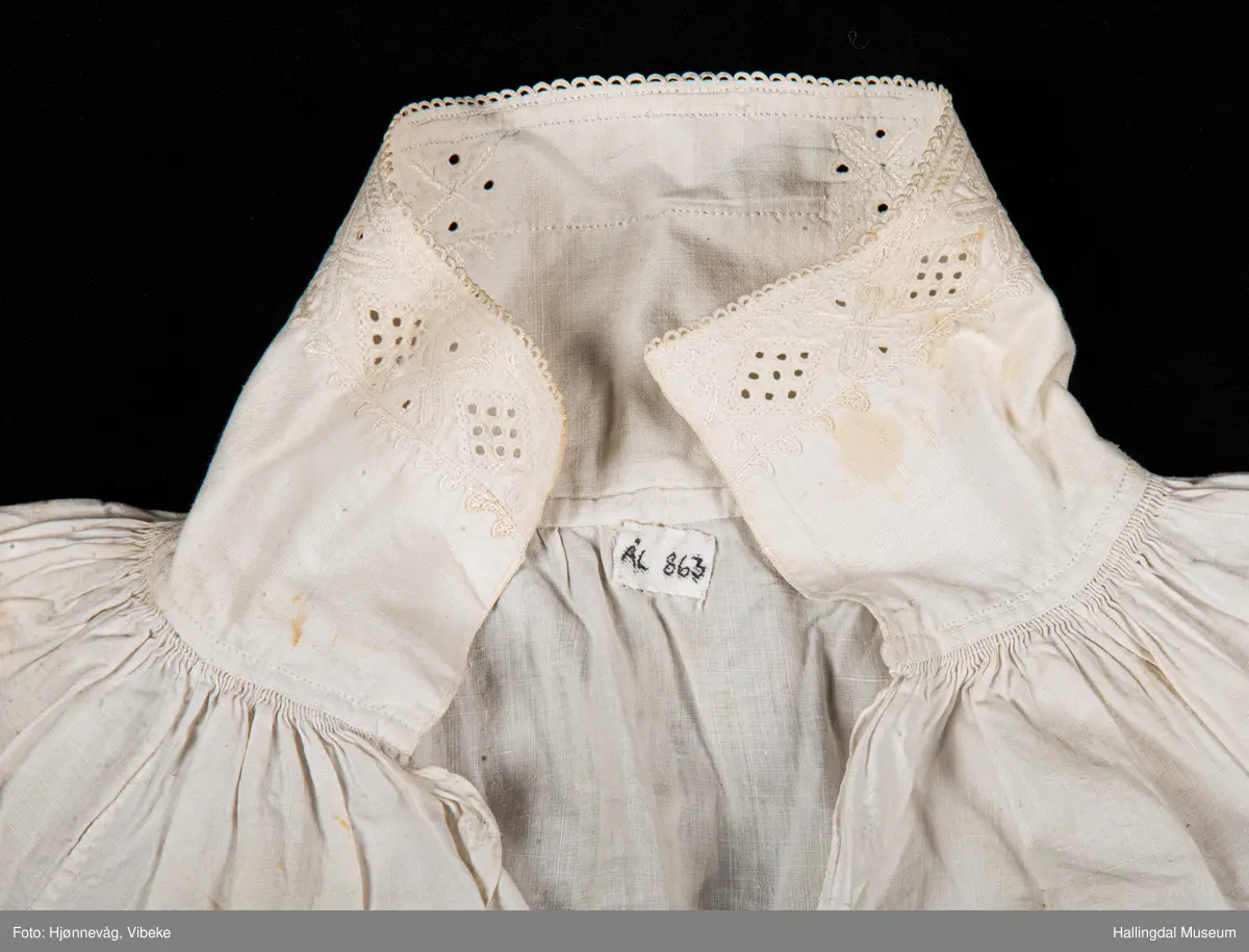 Rynket til halslinning. Kile ved skulder, rynket til halslinning, Erme rett ved skulder, rynket til mansjett. Kile under erme. Broderi i kvitsaum på linninger.