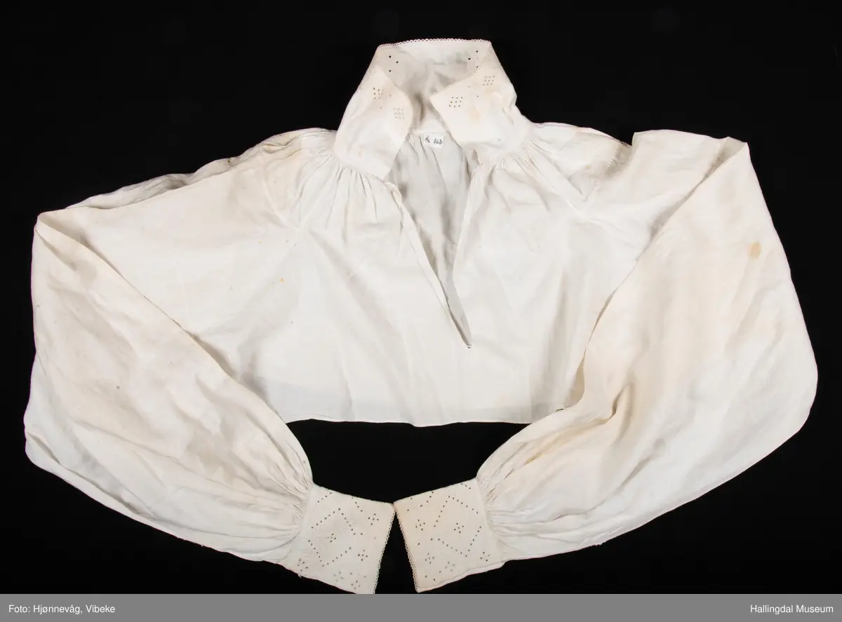 Rynket til halslinning. Kile ved skulder, rynket til halslinning, Erme rett ved skulder, rynket til mansjett. Kile under erme. Broderi i kvitsaum på linninger.