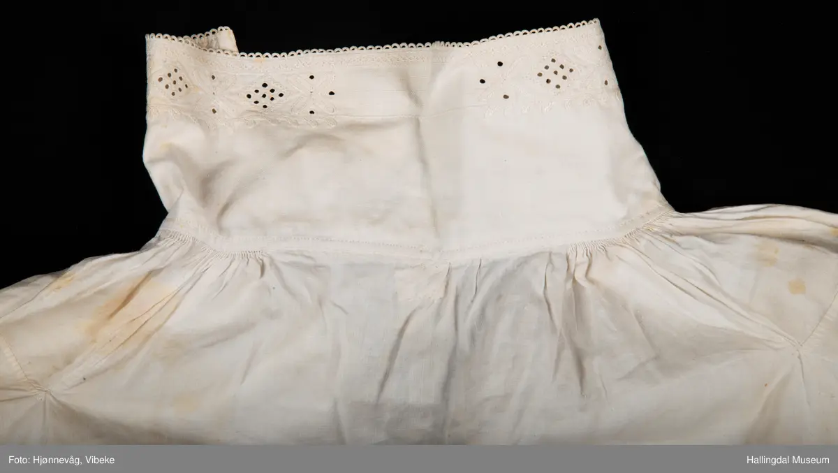 Rynket til halslinning. Kile ved skulder, rynket til halslinning, Erme rett ved skulder, rynket til mansjett. Kile under erme. Broderi i kvitsaum på linninger.