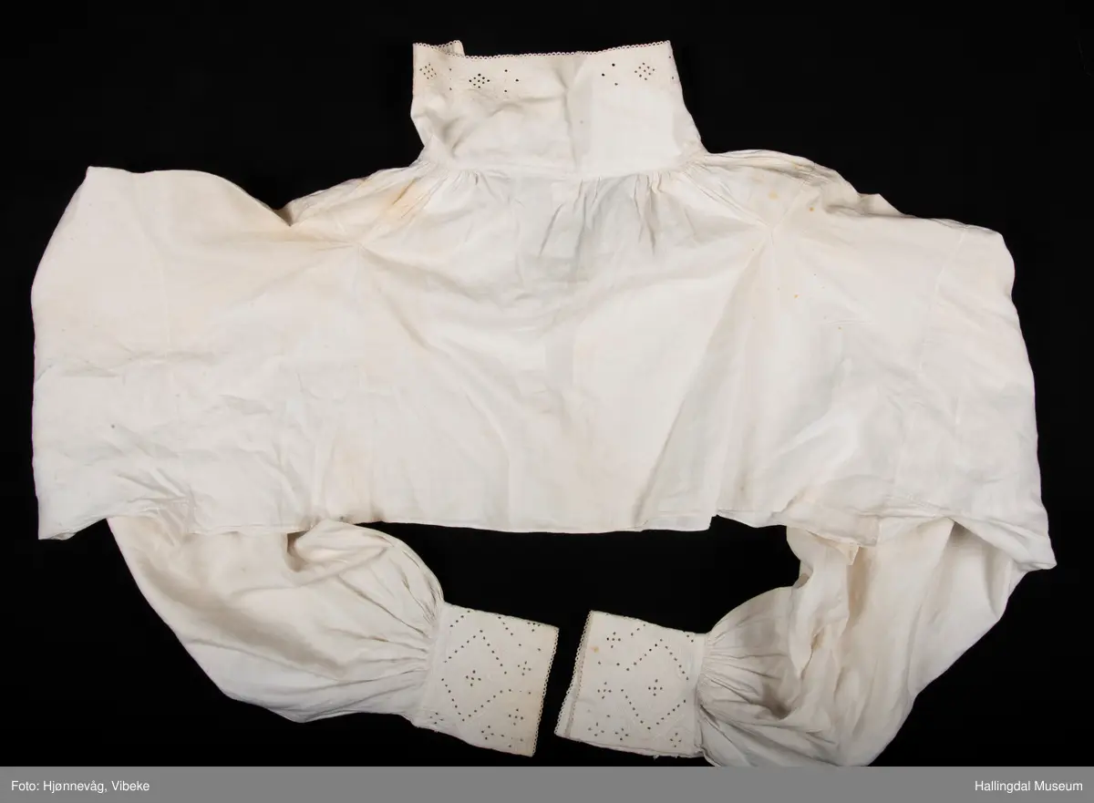 Rynket til halslinning. Kile ved skulder, rynket til halslinning, Erme rett ved skulder, rynket til mansjett. Kile under erme. Broderi i kvitsaum på linninger.