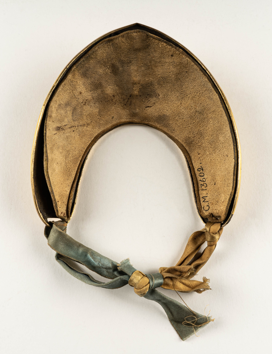 Dagofficersbricka, förgylld. Har tillhört kapten Th. Nordenadler, Högbo, Gästrikland.  Med Gustav III:s namnchiffer i ljusblå emalj. Dagofficersbrickan ingår i Gustav III:s uniform m/1779, för kaptener / kompanichefer för infanteriet.