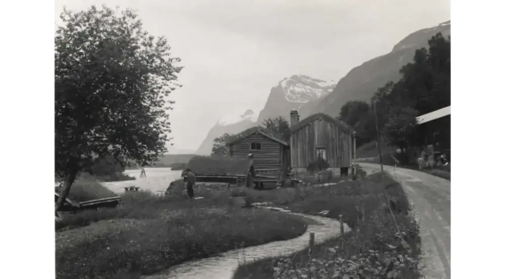 Gårdstun ved elva Driva med fjell i bakgrunnen, en vei går gjennom tunet.