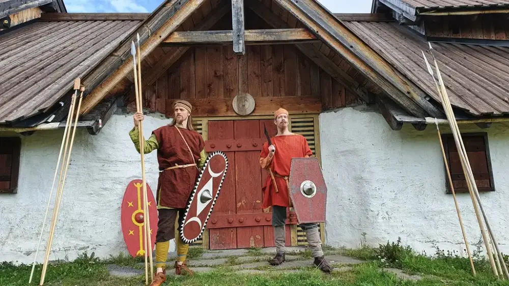 Foran langhuset stor to menn i romertidsklær og spyd og skjold i hendene
