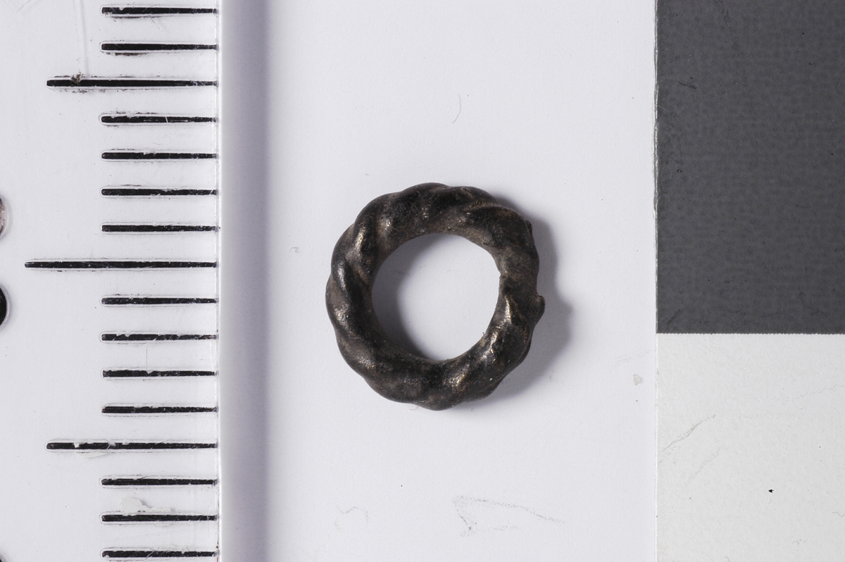 En svært liten metallring med bølgedekor som får overflaten til å se ut som tvunnet metalltråd.