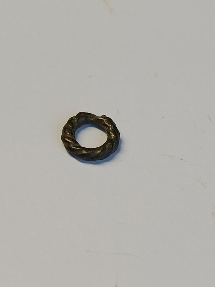 En svært liten metallring med bølgedekor som får overflaten til å se ut som tvunnet metalltråd.