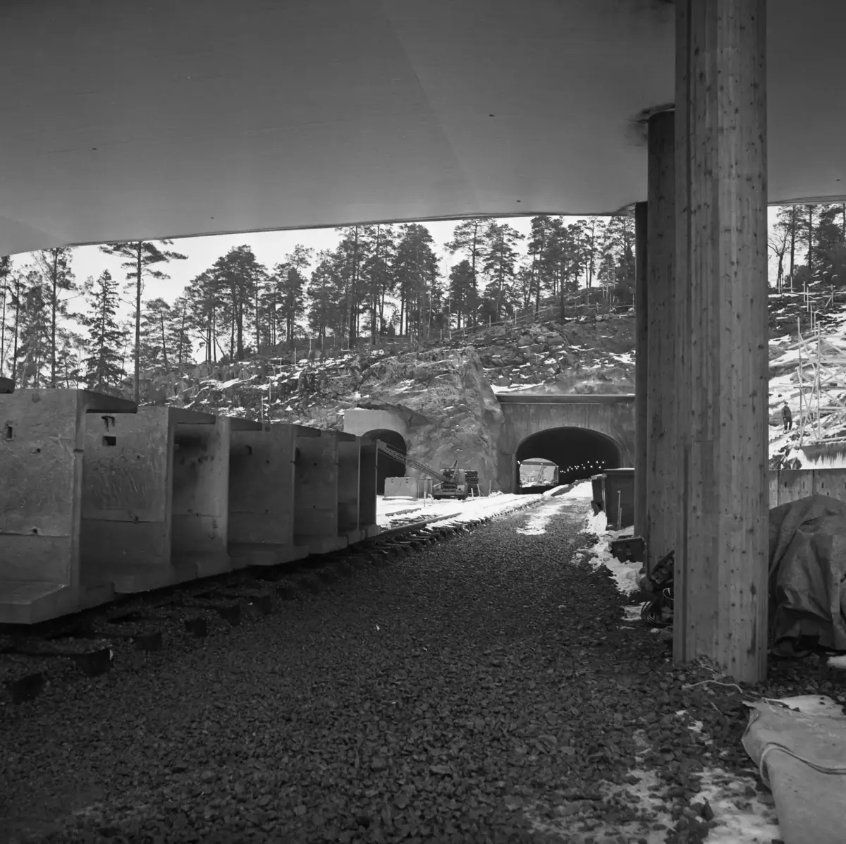 T-station Sätra år 1965!
Här byggs det för fullt trots januarikylan. Sätra är en förort i sydvästra Stockholm som bebyggdes under 60-talet. Stockholm stad köpte upp marken i området 1961 och 1964 började man bygga och fyra år senare var Sätra i det närmaste färdigställd. Det är ett område med blandad bebyggelse, i centrum finns affärer, skola och tunnelbanestation och några få höghus, sedan lamellhus grönska och parker. Ett steg längre ut från centrum i grönskan finns radhus och sist närmast vattnet ligger villorna. Tunnelbanestationen invigdes 16 maj 1965 och stationen fungerade som slutstation för linje 13 till 1 mars 1967. Stationen är lite unik då den är utrustad med vändspår och möjlighet till uppställning av trasiga tåg. Stationen är av denna anledning trespårig med två plattformar med ett mittspår och två sidospår. Från biljetthallen leder trappor och gångramp ned till varje plattform, gångramperna som vid byggandet var förberedda för eventuell installation av rörliga gångband. Centrumet består av ett överbyggt torg och var Stockholms första inomhuscentrum. Fotograf okänd.
