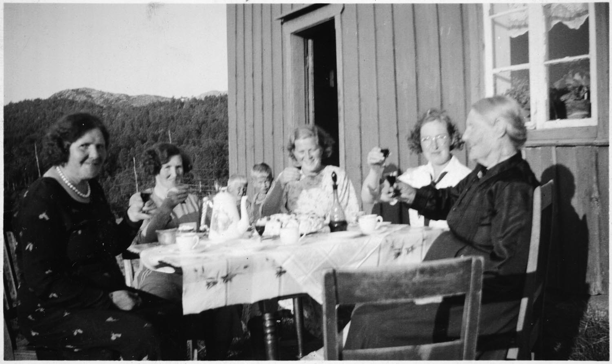 Leirfjord. Kaffebesøk utenfor huset, fem kvinner og to barn. Duker på bordet, bløtkake og fint kaffeservice. Ser ut som de skåler i noe som ant. er sterkere enn rød saft. Personene er ukjente.