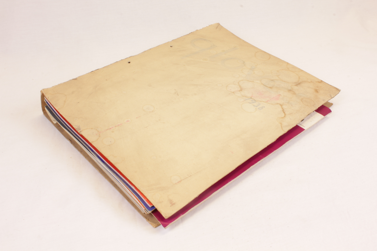 Årgang 1938 av bransjemagasinet "Gloves". Hjemmelaget "ringperm" som inneholder 14 blader som er gjennomhullet og festet sammen med tykk bomullstråd. Flere av bladene har papirbiter ilagt som bokmerke.