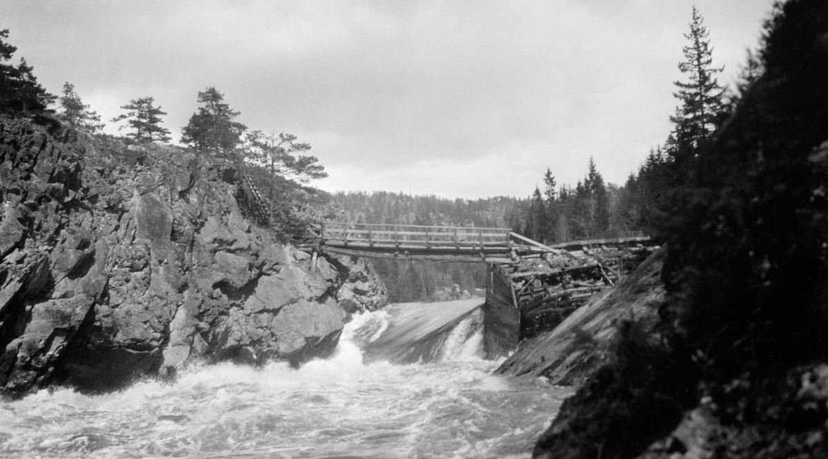 Den påbygde Sølvstudammen i Ågårdselva, fotografert under vårflommen i 1931. Bildet er tatt fra en bergkrent på sørøstre elvebredd med kameraet vendt mot strømretningen og dammen. Den var en forbygning av tømmer og planker (jfr. SJF.1989-04503, SJF.1989-04504 og SJF.1989-04505), som da dette fotografiet ble tatt var oversvømt av hurtigstrømmende vann. Over fossen og dammen lå det ei bjelkebru, lagd av rundtømmer, med rekkverk på den ene sida. Brua lå an mot en bergnabb på nordsida av vassdraget og mot et steinfylt tømmerkistekar med plankekledning på motstrøms side i den søndre enden. Trekonstruksjonene var preget av forfall.

Ågårdselva er en del av Glommas vestre løp gjennom daværende Tune kommune i Østfold. Denne elvesrekningen er cirka fem og en halv kilometer lang og renner fra den nordvestre enden av Isnesfjorden (Vestvannet) sørvestover gjennem berglendt terreng mot innsjøen Visterflo. Høydeforskjellen mellom Isnesfjorden og Visterflo er på bortimot 25 meter. Ågårdselva har tre fossefall, det øverste her ved Sølvstu, deretter ved Valbrekke og nederst ved Solli. Denne elvestrekningen ble ikke brukt som fløtingsled lenger da dette fotografiet ble tatt. I perioden 1906-1908 bygde nemlig Fredrikstad Tømmerdirektion i bruk en tømmertunnel gjennom berget fra Svartdal (fra da av også kalt «Toppen») ved Isnesfjorden til Eidet ved Mingevannet. I årene som fulgte ebbet virksomheten ved det en gang så store Sanne og Solli Bruk ut. Likevel hadde man sannsynligvis startet diskusjonen om bygginga av en ny Sølvstudam. Selskapene Borregaards og Hafslunds hadde nemlig gjort inngrep i Glommas østre løp, hovedløpet, som i lavvannsperioder gjorde det svært vanskelig å få tømmer som skulle til bedrifter nedenfor Sarpsfossen via Mingevannet, Isnesfjorden og den nevnte tømmertunnelen til Eidet gjennom det ovenforliggende trange sundet ved Trøsken. Dette forsøkte man å løse ved å heve vannspeilet i Isnesfjorden med en dam som skulle plasseres 10-15 meter ovenfor den eksisterende dammen ved Sølvstufossen.