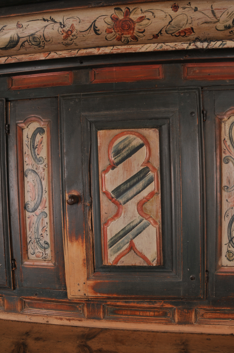 Øvre del har tre små skåpdører med ei hylle i kvar del. Nedre del har to store skåpdører med to hyller i kvar del. Rosemålinga er i grønt, raudt og kvitt. Kronelista er rosemåla på kvit botn. På venstre dørblad nede er det måla ein dansande figur og på høgre dørblad nede er det eit mannshovud. 