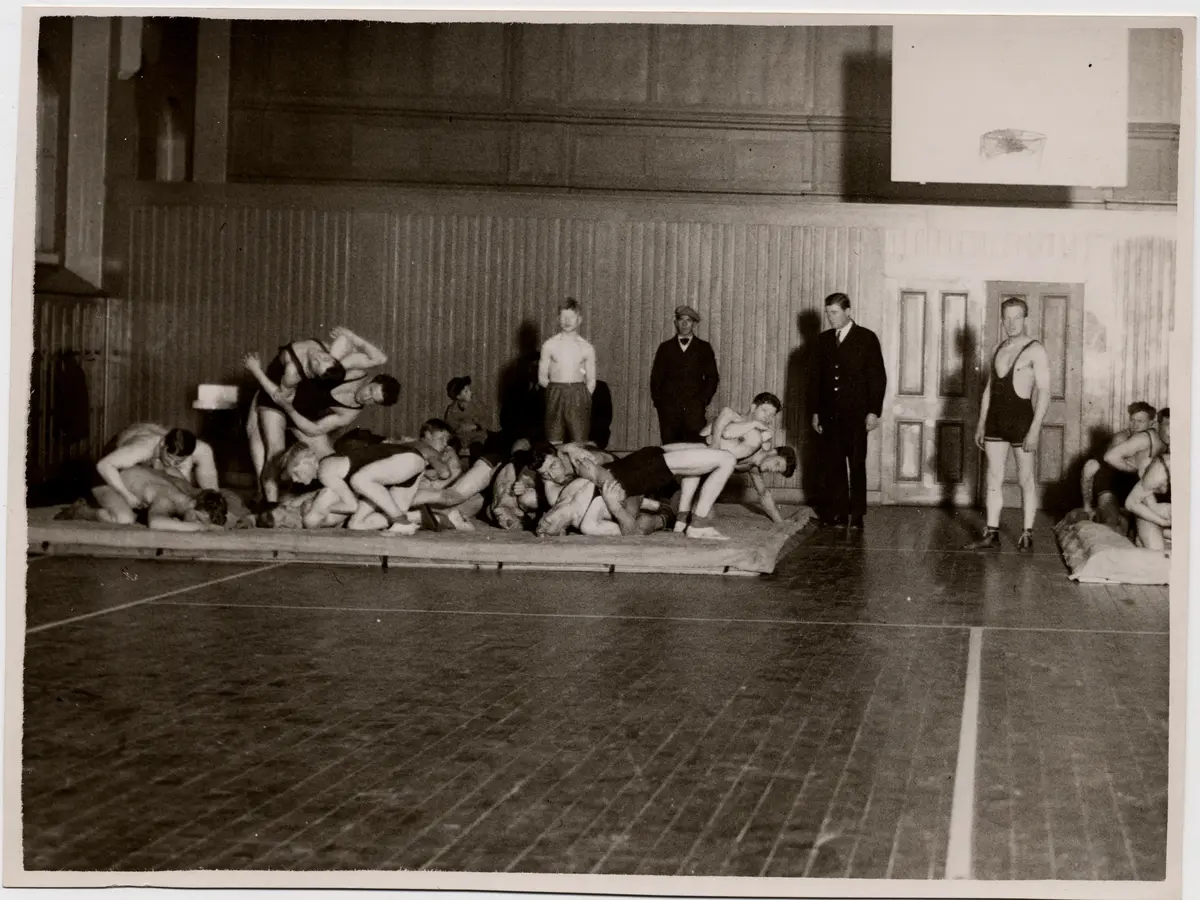 Ett femtontal brottare tränar på en matta, 1920-talet..   Exercishuset.

T.h. början på ytterligare en brottningsmatta.