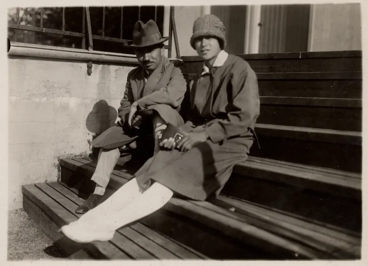 (Damolympiaden i friidrott 1926).   Slottsskogsvallen.

 En kvinna och en man med asiatiskt utseende sitter ensamma på ståplatsläktaren.

 Säkerligen Kinue Hitomi.