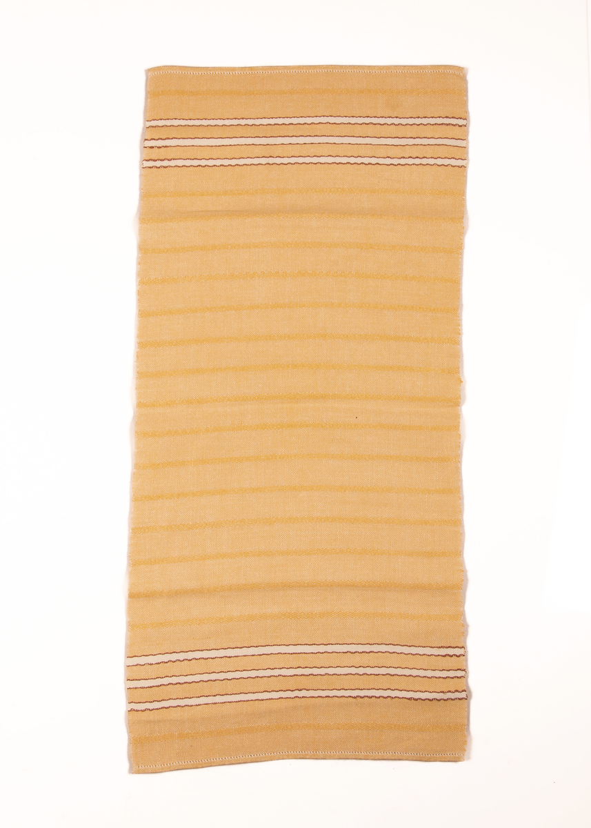 Gul løper med mørkegule striper ved inn i stoffet. 3 hvite border med brun kant i hver ende. Faldet med hullsøm.