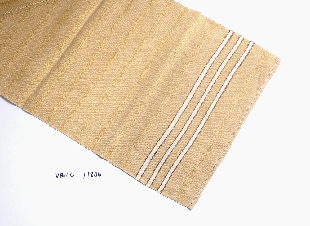 Gul løper med mørkegule striper ved inn i stoffet. 3 hvite border med brun kant i hver ende. Faldet med hullsøm.