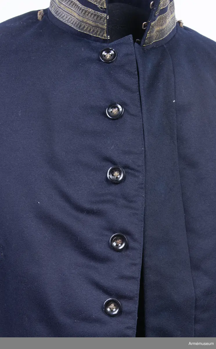 Blåsvart kollett med ståndkrage och guldgaloner.

Kolletten är sydd av blåsvart fint kläde med dold knappstolpe med enkelknäppning. Den knäpps med sju svarta knappar av metall med motsvarande knapphål. Nertill i midjan finns i vänster framstycke en "tunga" i midjan som knäpps överlappande på höger framstycke. Plagget är lätt vadderat upptill både fram och bak, och är fodrat med svart tunt sidentyg.
Kolletten är kroppsnära och midjekort och konstruerad med två framstycken, två sidstycken bak, samt bakstycke med delsöm mitt bak. Den har ett litet skört bak med två utstående "korvar". Ärmarna är smala tvåsömsärmar med ärmuppslag i samma färg.
Plagget har uppstående krage med påsydd dekoration av dubbel metallgalon, samt metallgalon och guldfärgad knapp nertill på ärmarna. Ärmsprunden knäpps med två guldfärgade mindre knappar. En knapp saknas i vänster ärmsprund. Samtliga guldfärgade knappar pryds av tre kronor på räfflad botten, med smal slät rand runtom.
På axlarna sitter rester av tråd som visar att plagget troligen har haft någon form av axeltränsar. På vänster sida av bröstet finns två sydda tränsar för att fästa ordnar eller utmärkelser i.