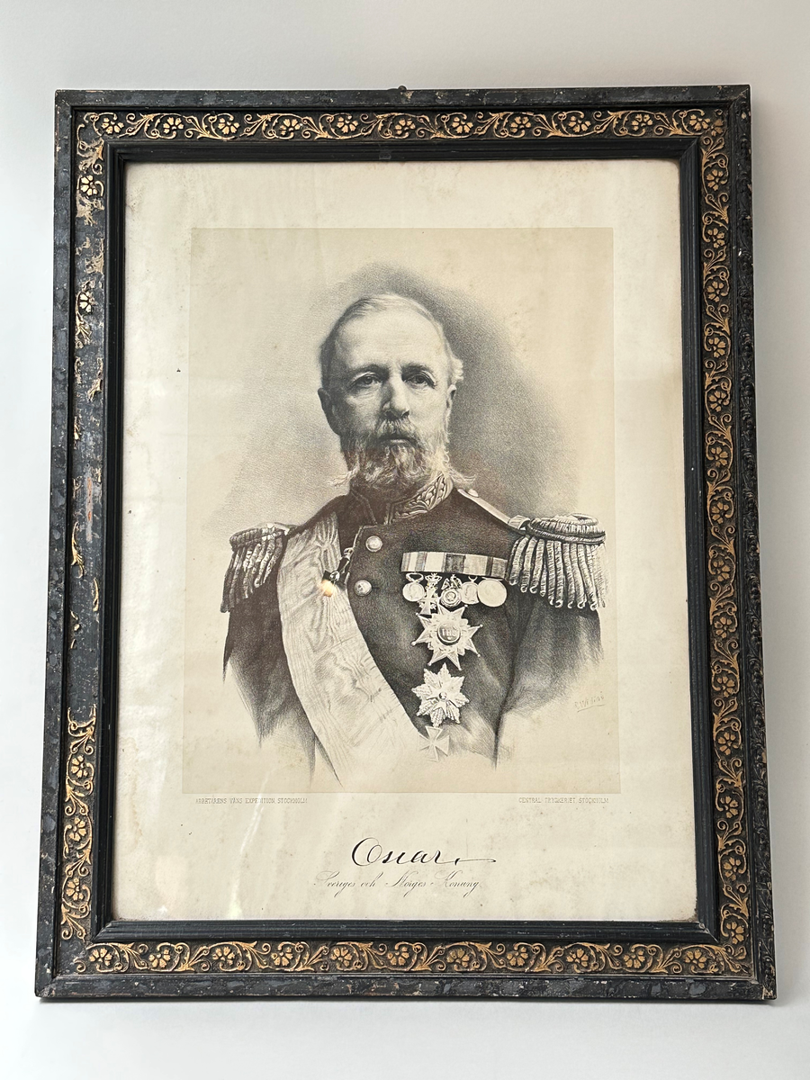 Tavla av Oscar II. Svart ram med guldbronserade blommor, akantusornamentik. 