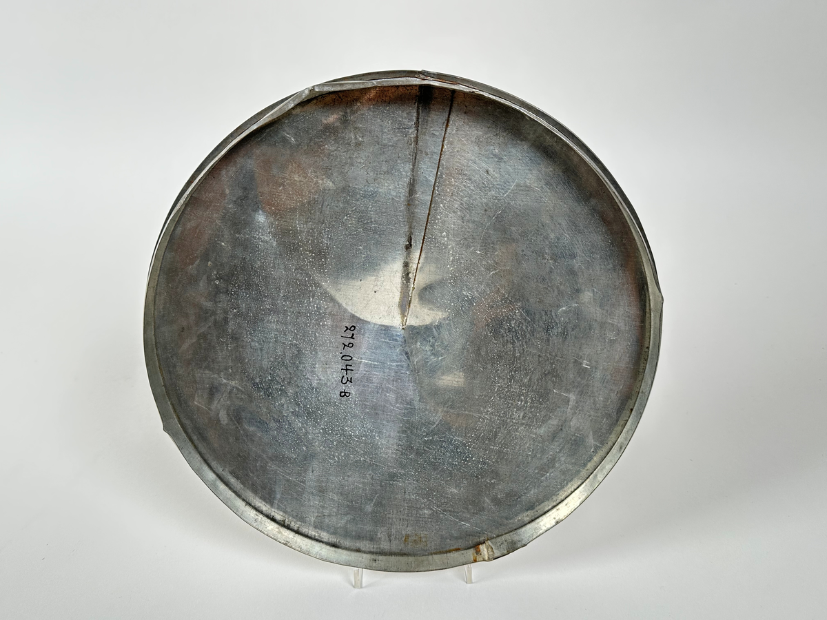 Plåtlock till cistern. Plåten formad i en cirkel vars radie klippts och kanten vikts över, vilket gör locket lätt konformat. Handtag av tunn plåtremsa, vikt utåt, nära lockets ytterkant. 