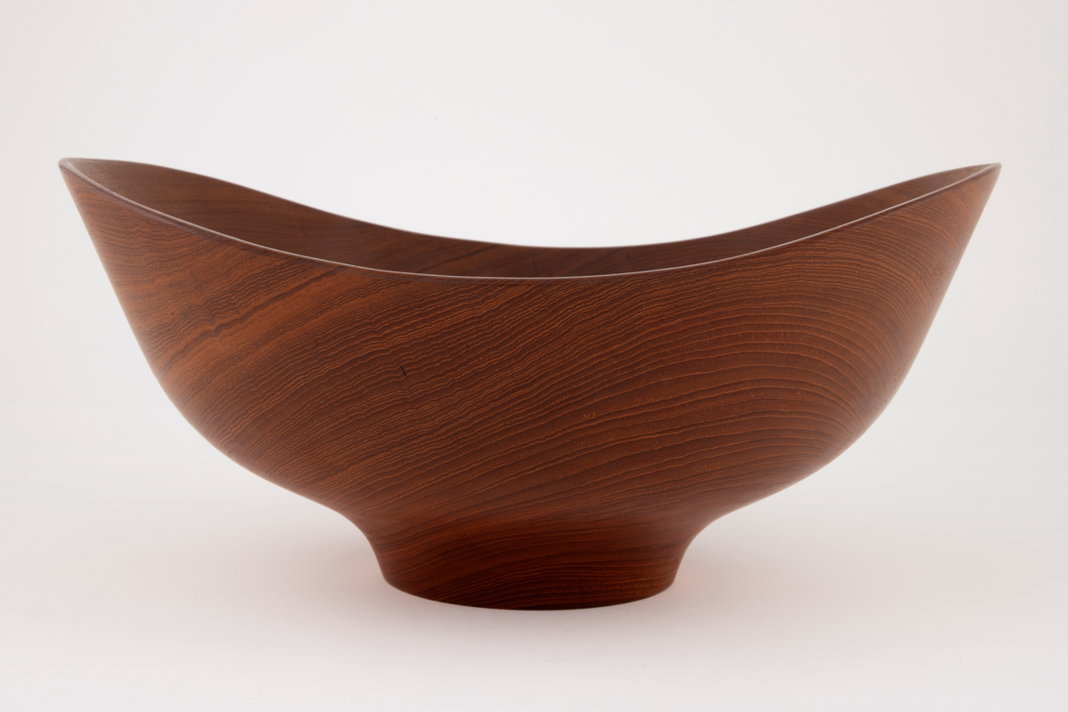 Skål i teak. Stor, dyp, oval form med liten, lav, sirkelrund fot. Skålen har skrånende sider som er høyest på kortsidene. Konsentriske årringer noe forskjøvet i forhold til skålens sentrum. På fotens underside er det tre gjenpluggede hull etter dreieskivens tapper.