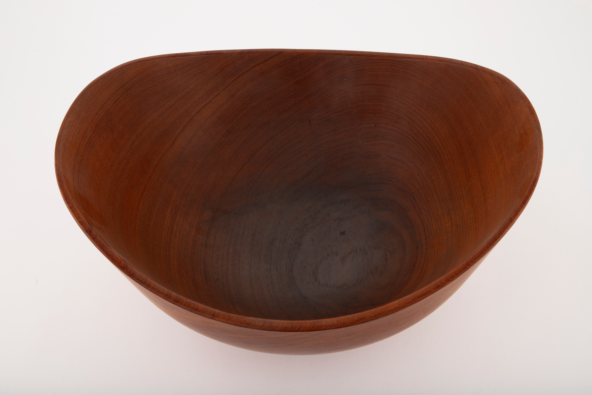 Skål i teak. Stor, dyp, oval form med liten, lav, sirkelrund fot. Skålen har skrånende sider som er høyest på kortsidene. Konsentriske årringer noe forskjøvet i forhold til skålens sentrum. På fotens underside er det tre gjenpluggede hull etter dreieskivens tapper.