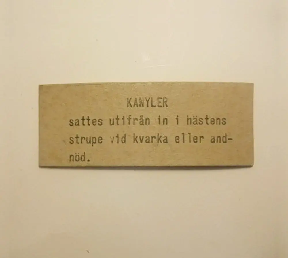 Etikett till utställning om sjukvårdsföremål till hästar under hästspårvagnarnas tid. Texten säger:
"KANYLER sattes utifrån in i hästens strupe vid kvarka eller andnöd". Storlek = 10,5 x 4 cm