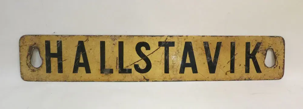 På andra sidan av skylten, text Stockholm.

Hallstaviks station invigdes 1915 som den norra ändpunkten i en förlängd del av den smalspåriga Rimbo-Sunds Järnväg (RSJ). RSJ blev sedermera uppköpt av och inlemmat i Stockholm-Roslagens Järnvägar (SRJ) som förstatligades 1959.

I Roslagen började man på 1960-talet att lägga ned allt fler linjer som man inte ansåg var tillräckligt lönsamma. Detta innebar bland annat att man fr.o.m. den 25 september 1966 nedlade persontrafiken Rimbo-Hallstavik.


