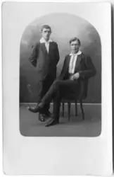 Vykort med ateljéporträtt av två yngre män. På baksidan står