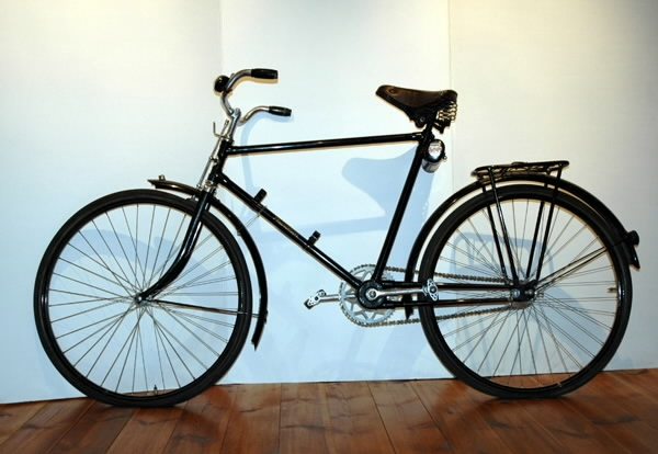 Cykel av stålrör. Diamond-ram utan bakstag, med dubbel bakgaffel. Spiralfjädrad terrysadel av läder. Styrhandtag celluloidklädda, svarta. Ringklocka med ett eklöv och ett ollon inom var sin sexkantig ram, samt namnet "PHÄNOMEN" i relief. Handbroms verkande på framdäckets ovansida. Lykthållare. Cylindrisk vertygslåda av plåt på sadelröret. Pakethållare på fyra stag, som konvergerar i bakgaffeländarna. Fjäderklämmor för pump på nedre ramröret. Omfångsrik vevlagerhylsa. Kattöga. Styre och framgaffelkrona förkromade. I övrigt svart lackering med smala, gula och blå linjer och bred gul rand i fälgarnas mitt. På styrrörets framsida runt, vitt fält med text: "PHÄNOMEN-WERKE GUSTAV HILLER A.G. ZITTAU" och i centrum sexkantigt, mörkblått fält med: "PHÄNOMEN" i guldskrift. På vertygslådans lock: "PHÄNOMEN SCHWINGRAD" i rött, blått och vitt.