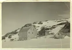 Ein gard med eit stort bolighus, i eit fjellandskap dekt av 
