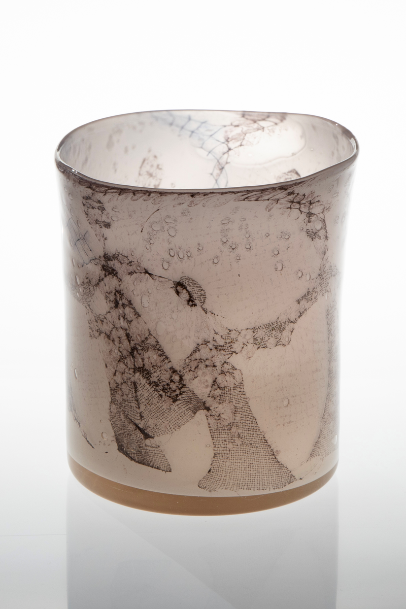 Høyreist ovalformet vase i grårosa glass med innlagt dekor av metallnett. Dekoren fremstiller stiliserte kvinnefigurer i en dansende bevegelse. Øvre del er svakt konisk og har en ujevn formet munningsrand.