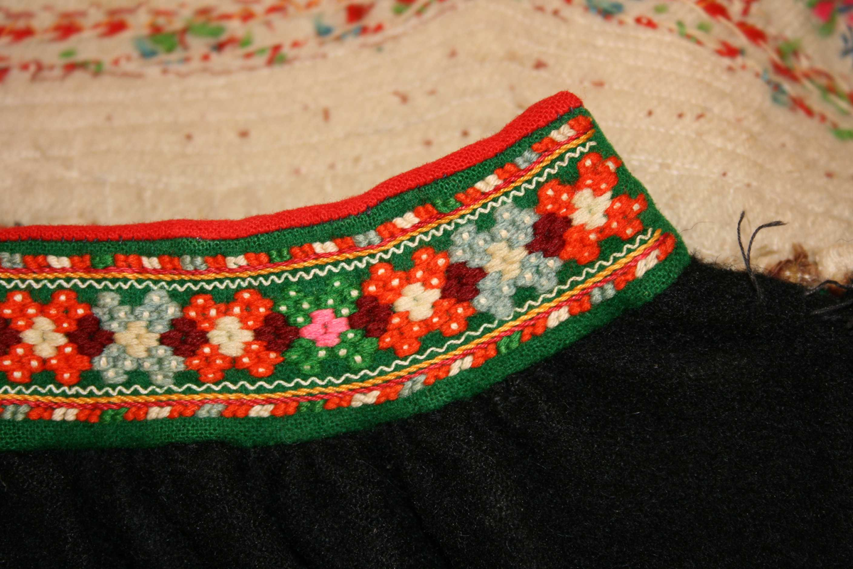 Svart vadmålsstakk med selar og broderi.