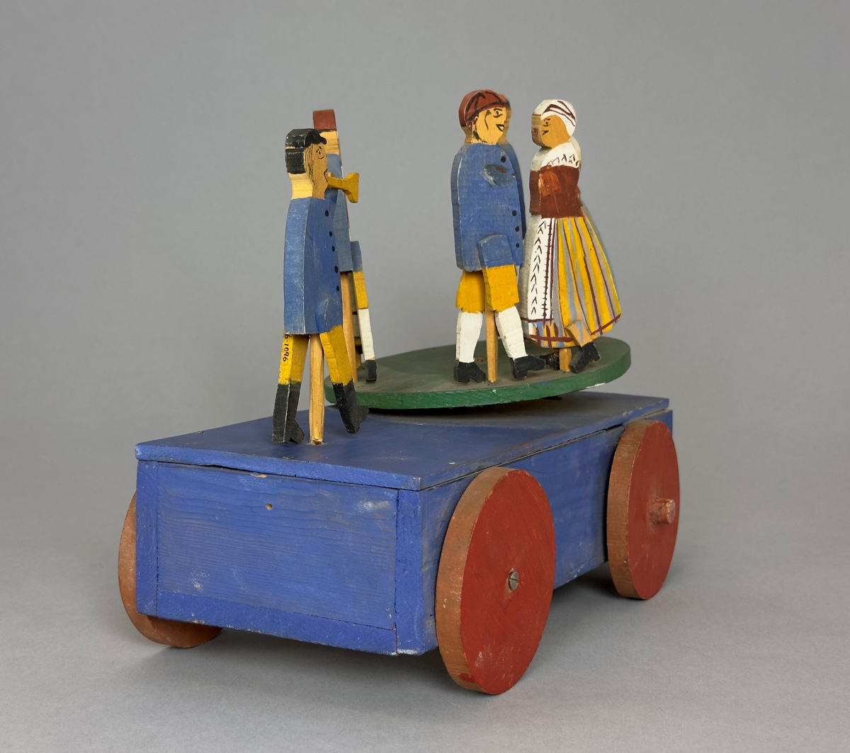 En blå kärra med röda hjul och grön dansbana med tre dansande par. Innuti ett "maskineri", som gör att banan snurras då kärran rullas.