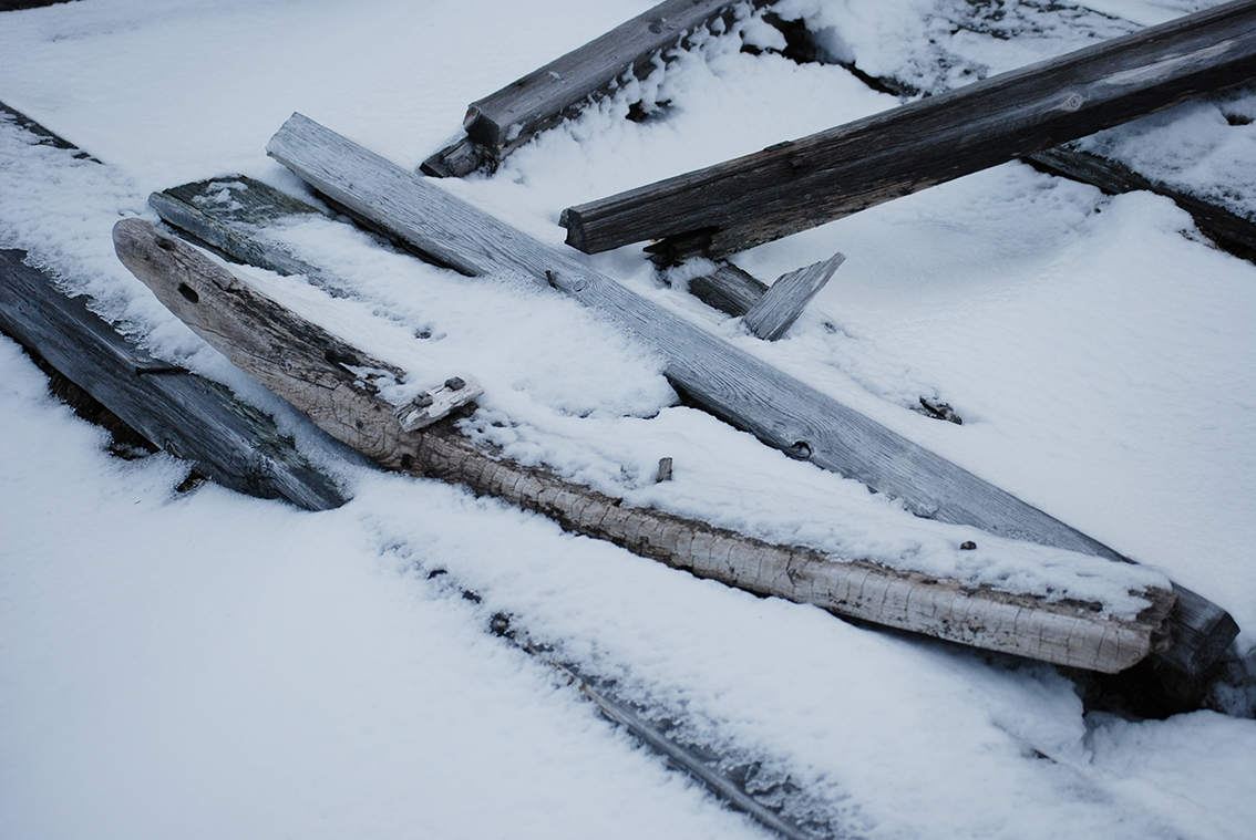 En med från en kälke bland brädvirke i snö.